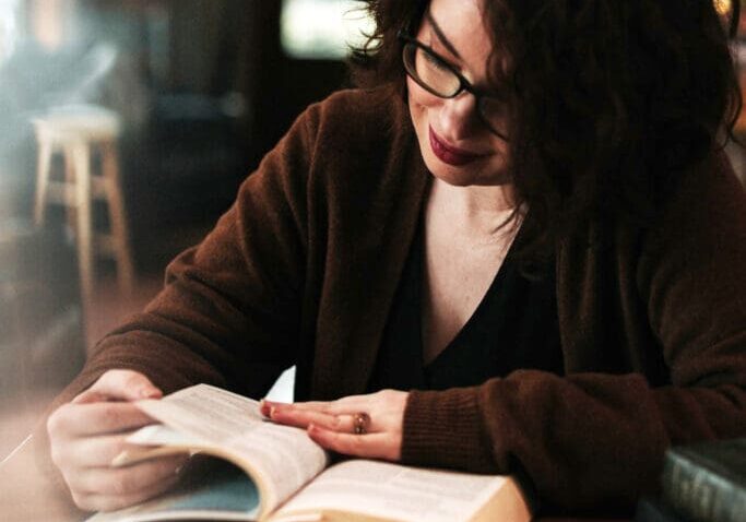 A woman sitting at a table reading a book.